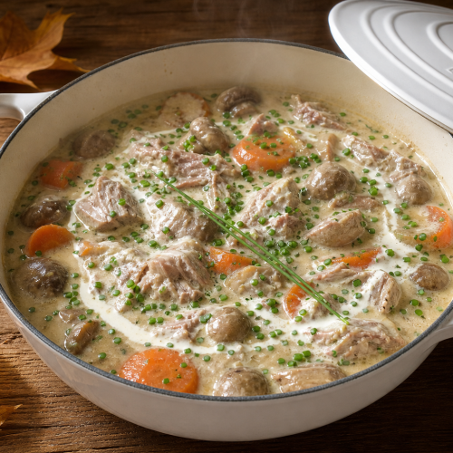Blanquette de veau céto dans une cocotte blanche, sauce crémeuse, champignons et ciboulette, sur table en bois