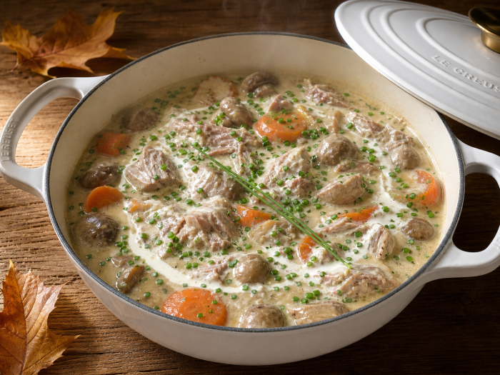 Blanquette de veau céto dans une cocotte blanche, sauce crémeuse, champignons et ciboulette, sur table en bois
