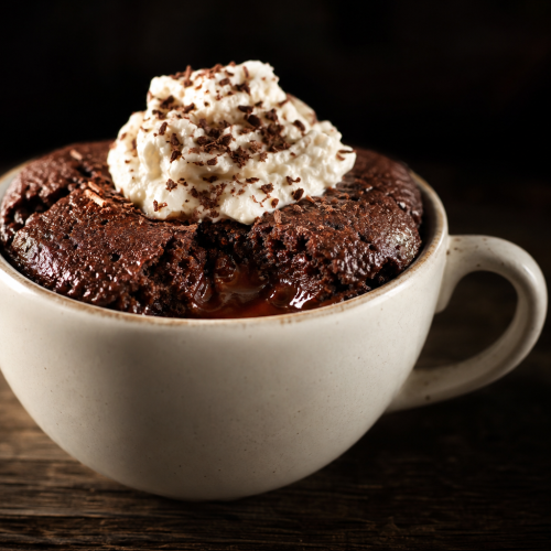 Mug cake au chocolat cétogène avec crème fouettée et copeaux de chocolat dans une tasse blanche sur une table en bois