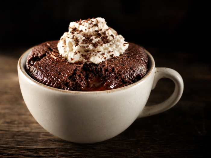 Mug cake au chocolat cétogène avec crème fouettée et copeaux de chocolat dans une tasse blanche sur une table en bois