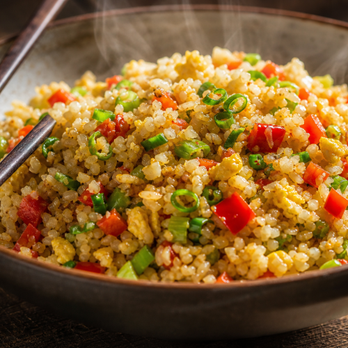 Bol de riz de chou-fleur sauté aux légumes et œufs, avec oignons verts et huile de sésame, sur fond en bois.