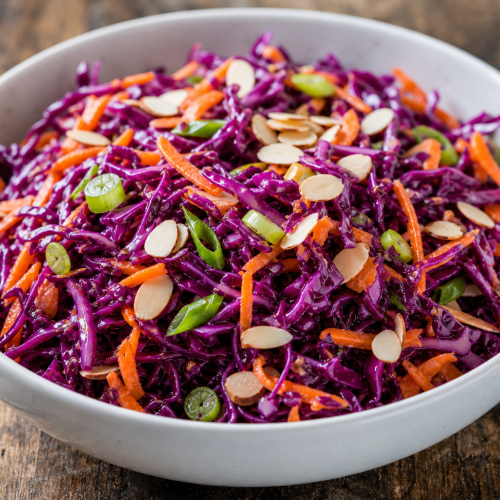 Salade de chou rouge céto avec carottes râpées, oignons verts et amandes dans un bol blanc