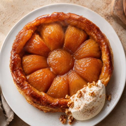 Tarte tatin keto aux pommes caramélisées, démoulée dans une assiette blanche, avec une boule de crème fouettée.