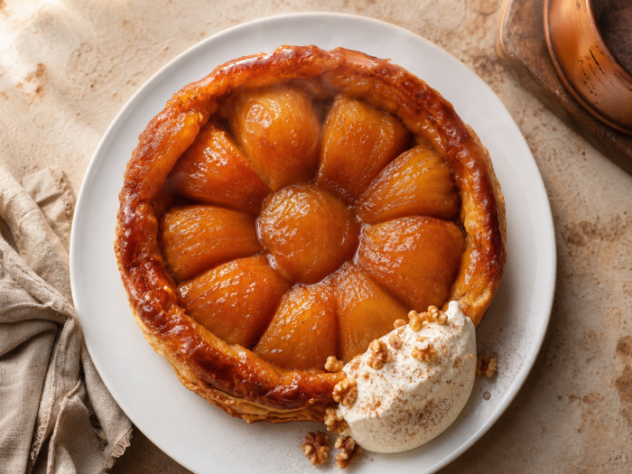 Tarte tatin keto aux pommes caramélisées, démoulée dans une assiette blanche, avec une boule de crème fouettée.