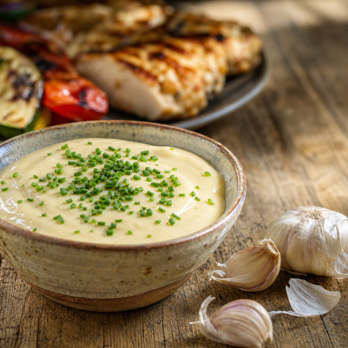 Bol de sauce à l'ail kéto crémeuse, garnie de ciboulette fraîche, sur une table en bois rustique.