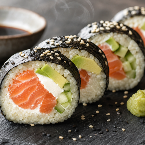 Sushis keto sans riz, à base de purée de chou-fleur, garnis de saumon, d’avocat et de concombre, enveloppés de nori.